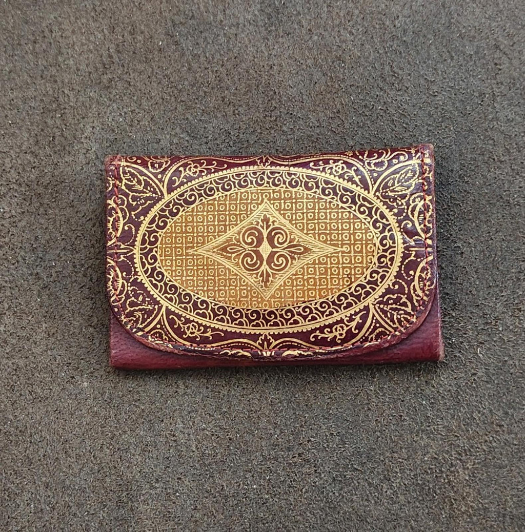 Small coin purse wallet with burgundy leather backing and gold ornate oval emblem front.