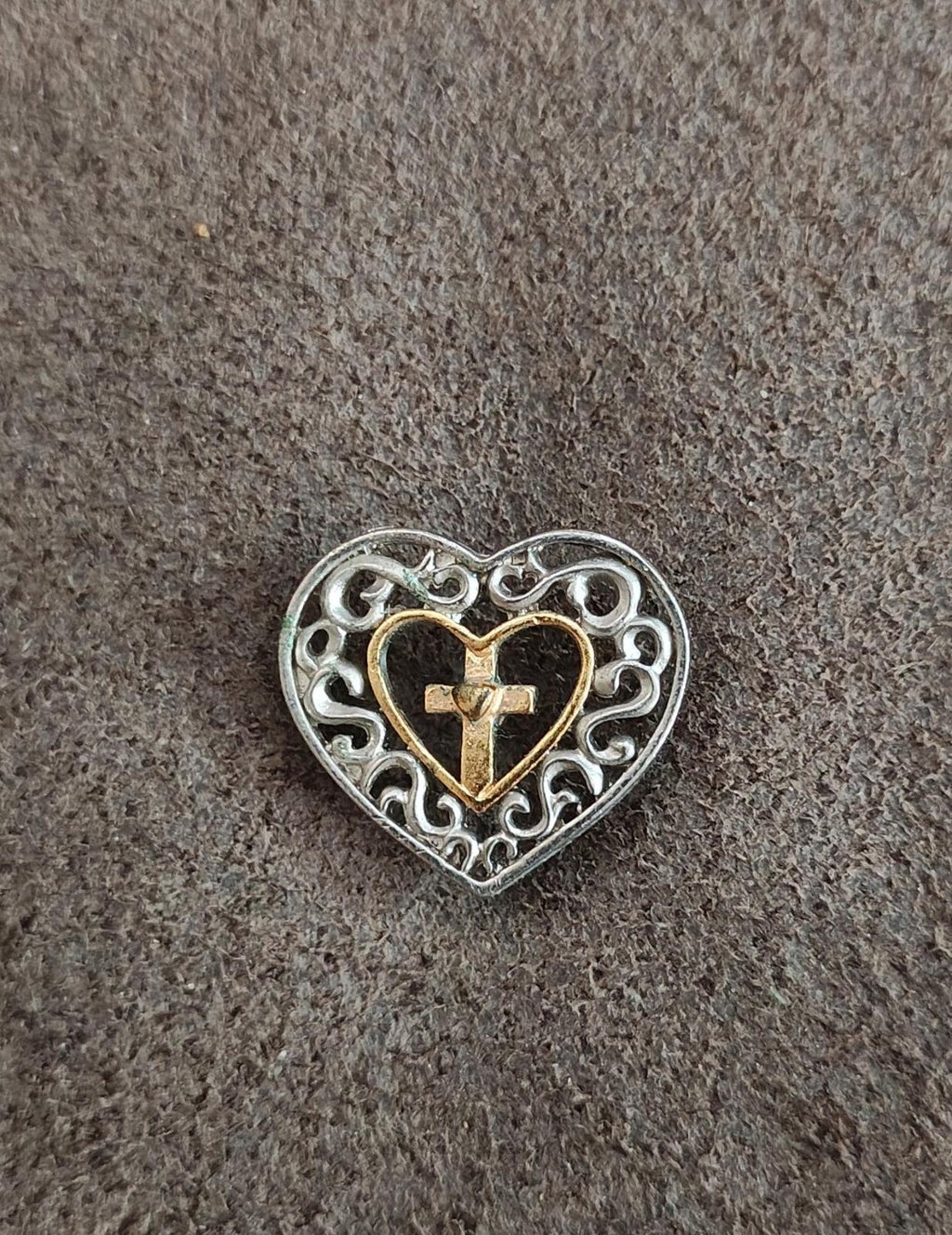 Heart cross pin on textured surface, silver-toned filigree with gold-toned heart cross