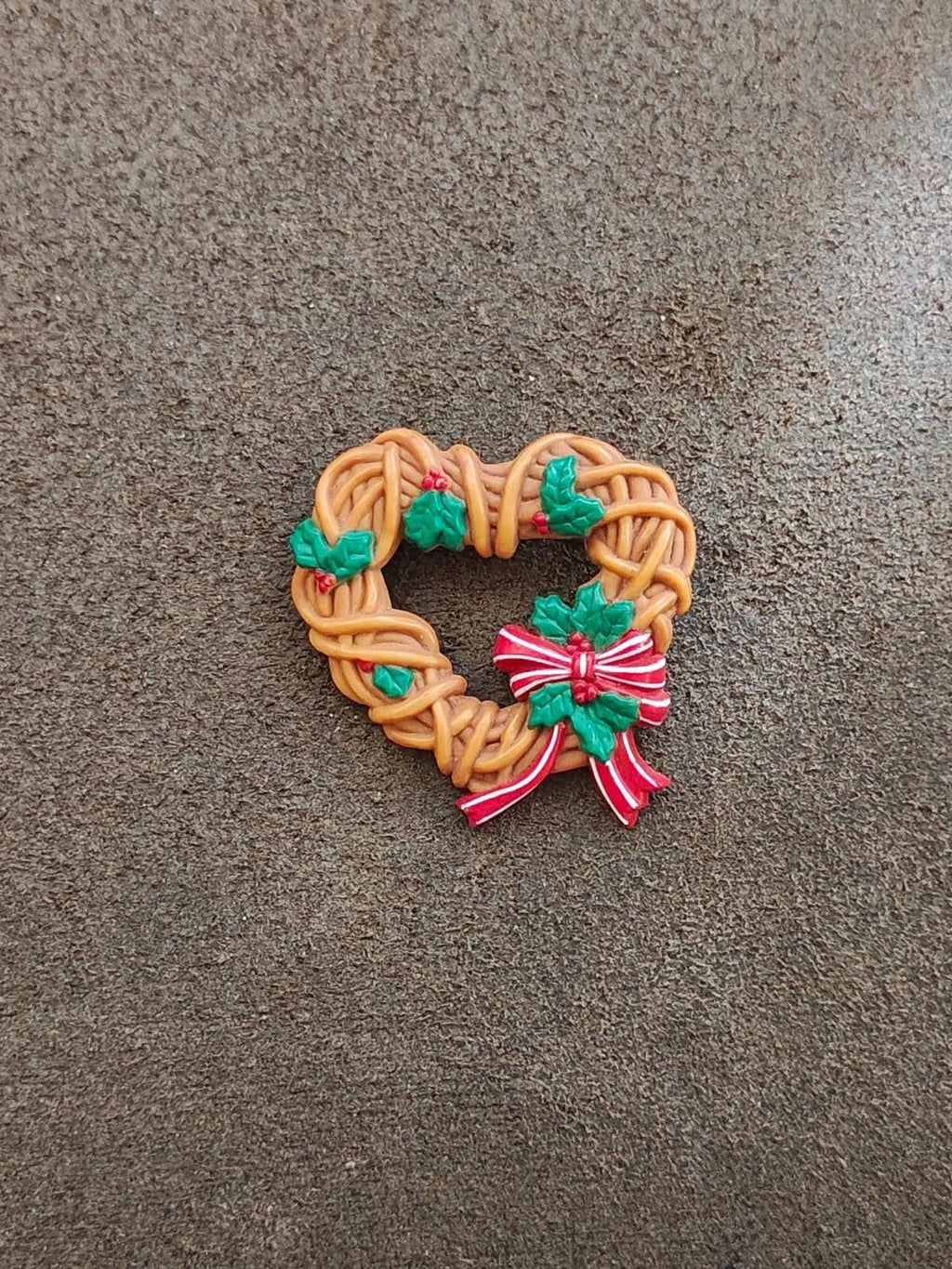Heart-shaped Christmas wreath brooch with brown braided edges, green holly, red ribbon bow