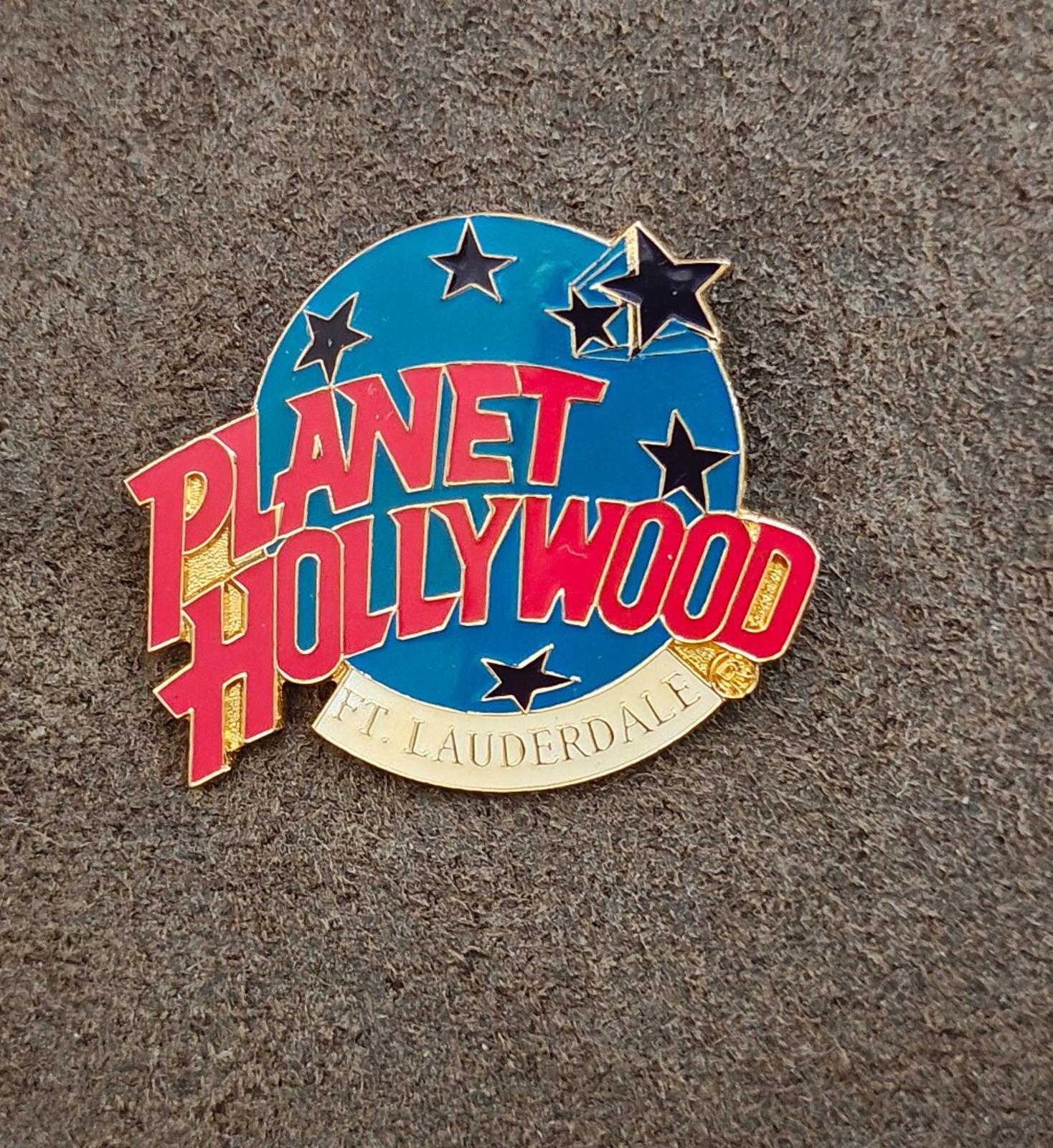 Blue enamel lapel pin with red Planet Hollywood lettering, star accents, gold rim.
