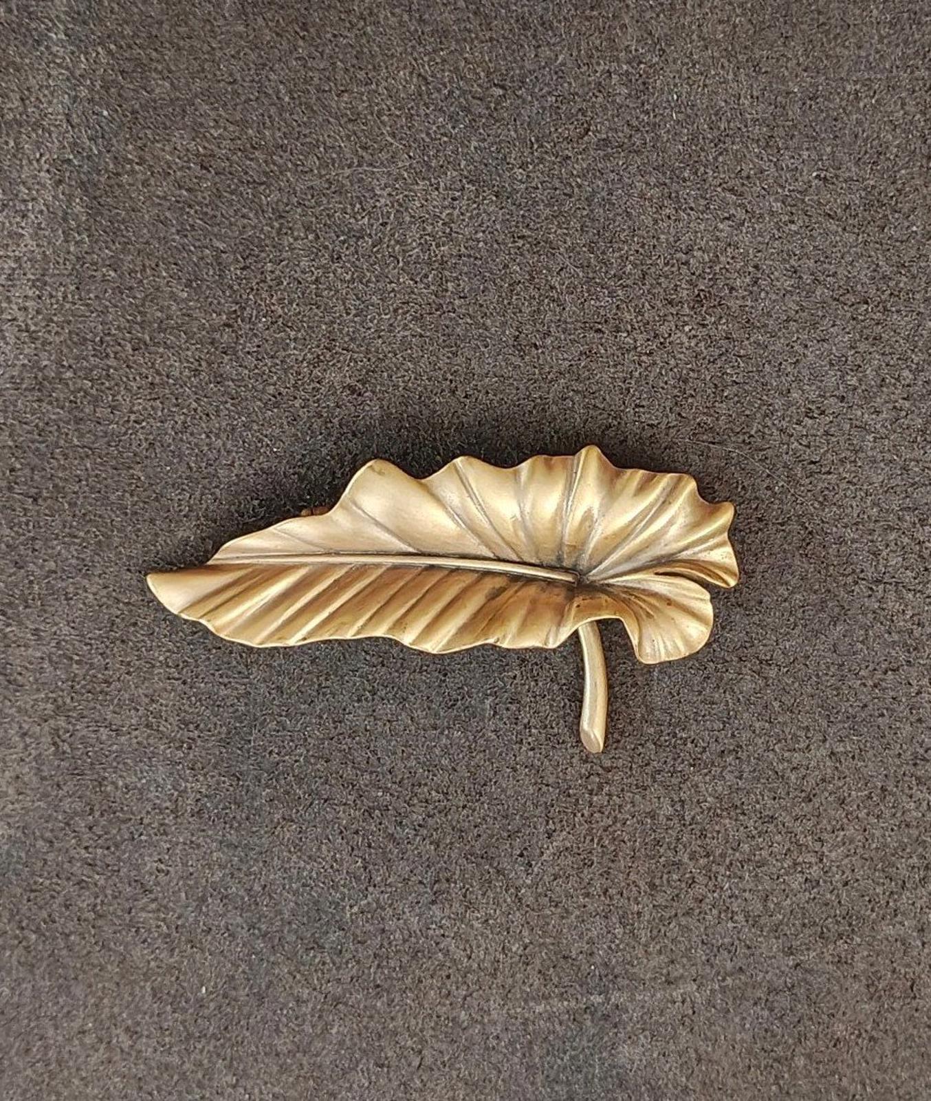 Gold-tone leaf brooch pin showing vertical pin stem and ridged leaf texture.
