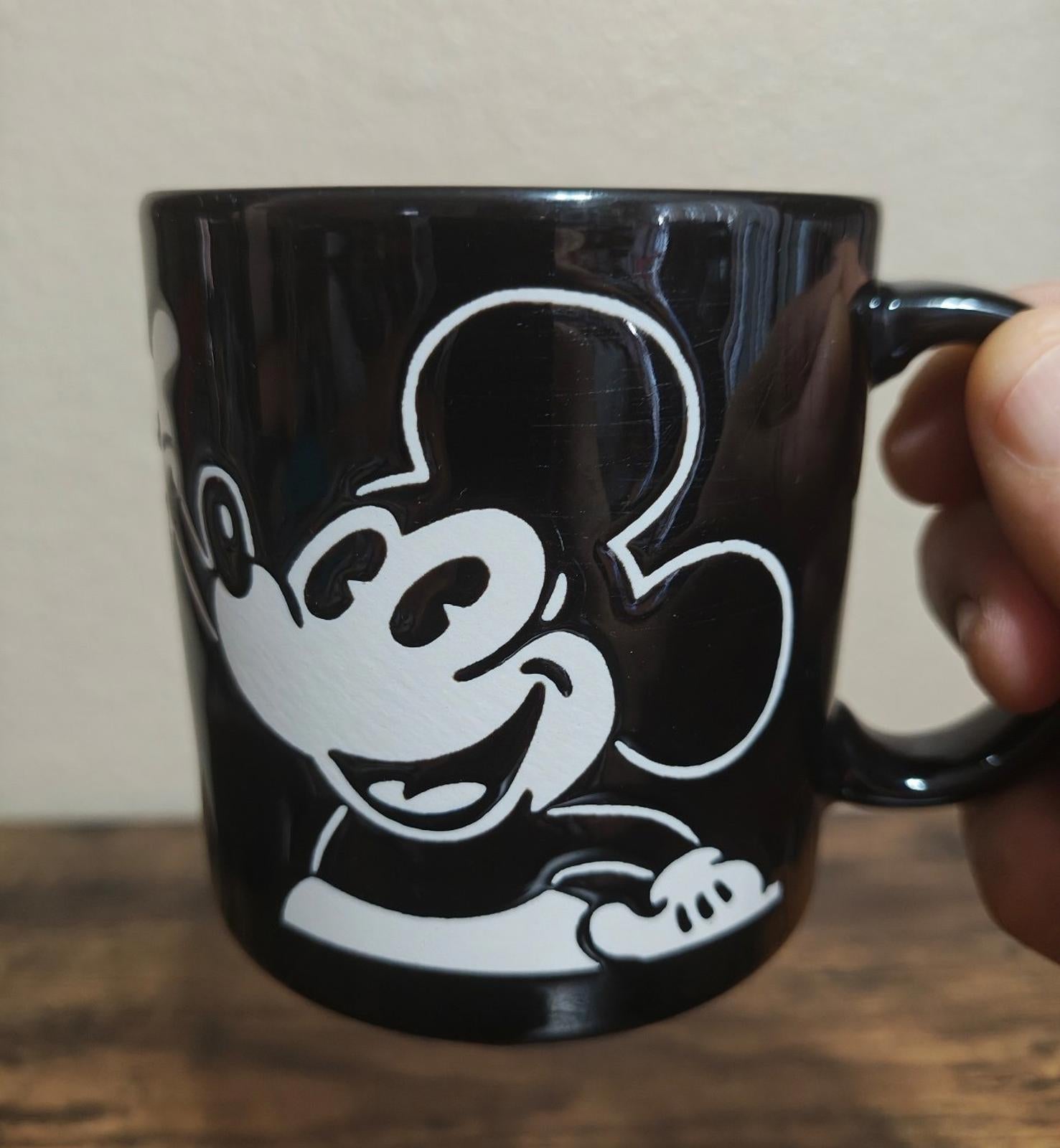 Black mug close-up with white Mickey Mouse “pie eyed” style graphic and handle