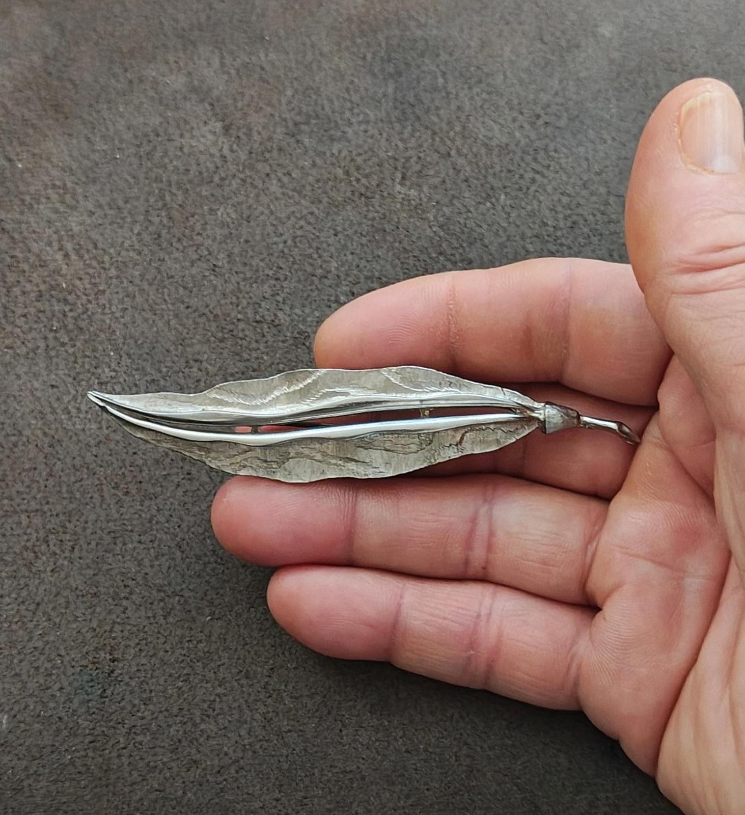 Silver leaf brooch held in hand, hammered finish with curved lines and pin closure