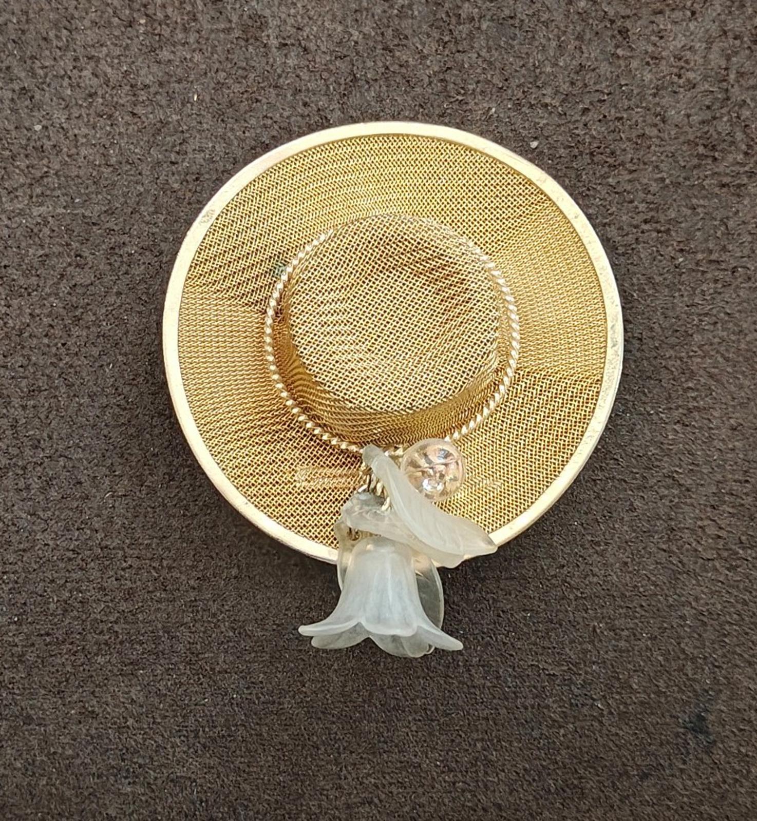 Gold-tone mesh sun hat brooch pin on dark surface with white angel charm below