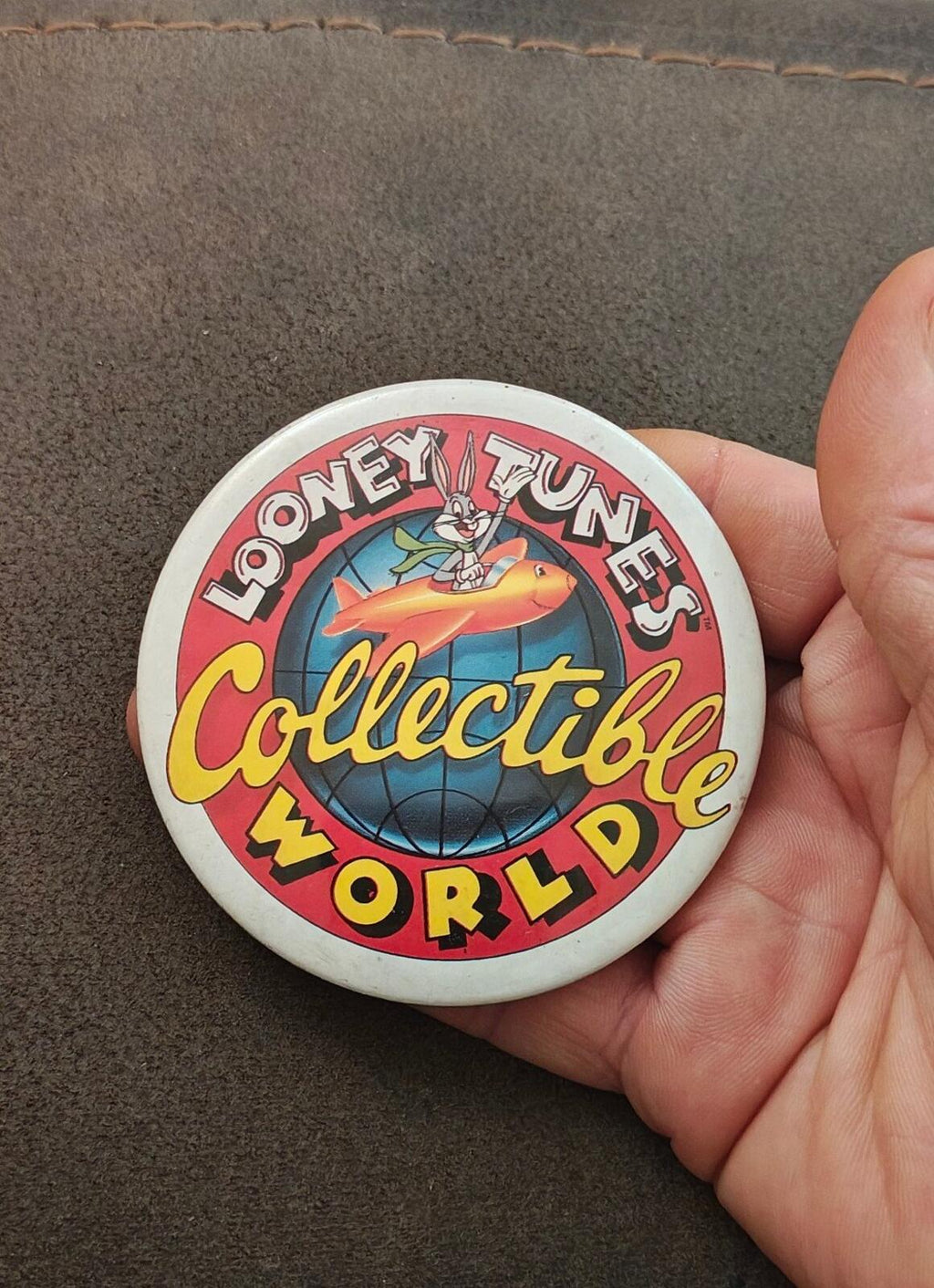 Round Looney Tunes “Collectible World” button pin in hand, with rocket character graphic (red/blue).