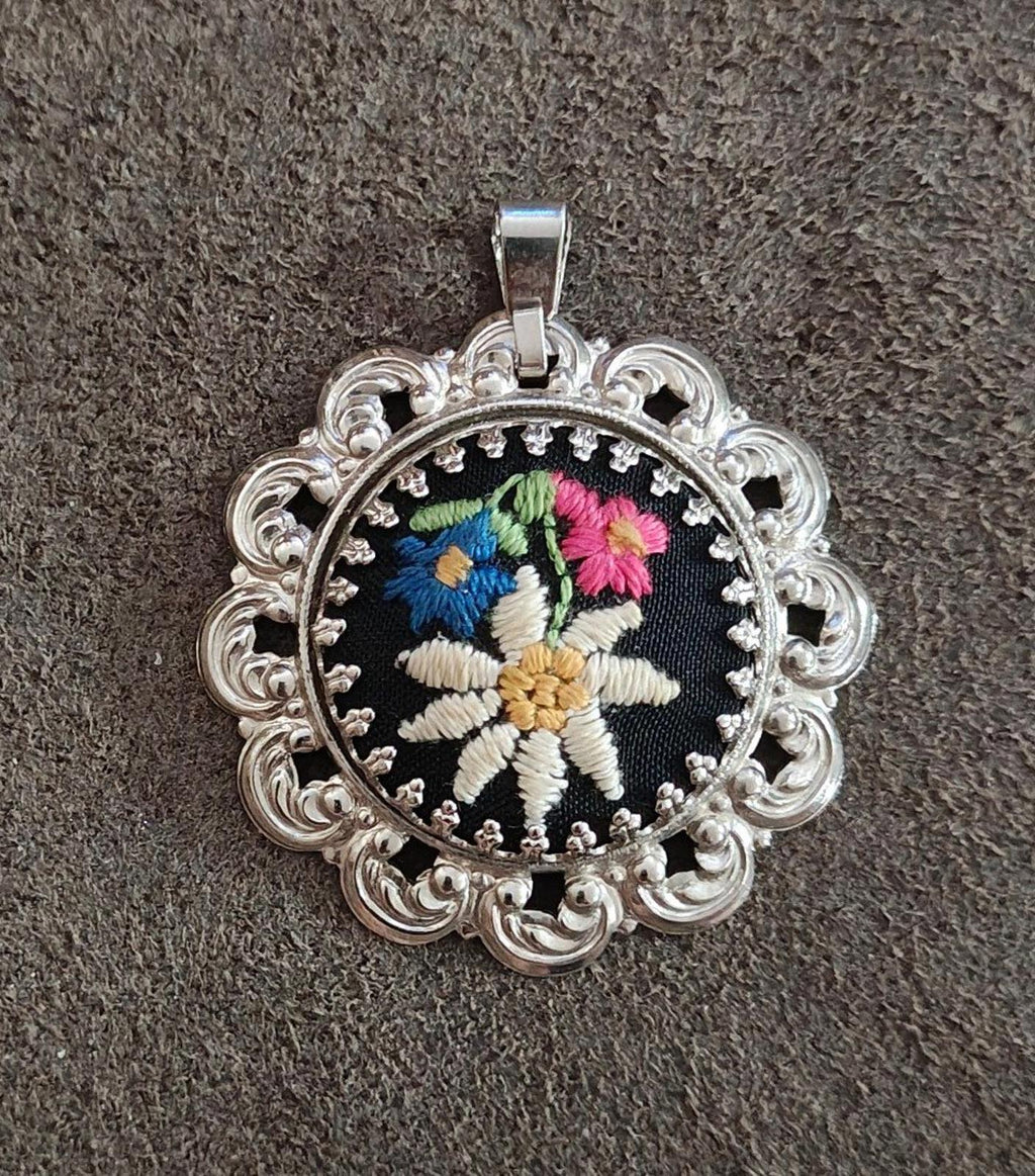 Silver filigree round pendant with black fabric and stitched white and colored flower.
