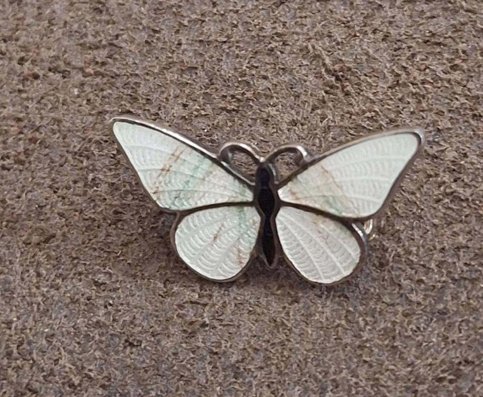 Enamel butterfly pin brooch with pale white wings and dark central body on fabric.
