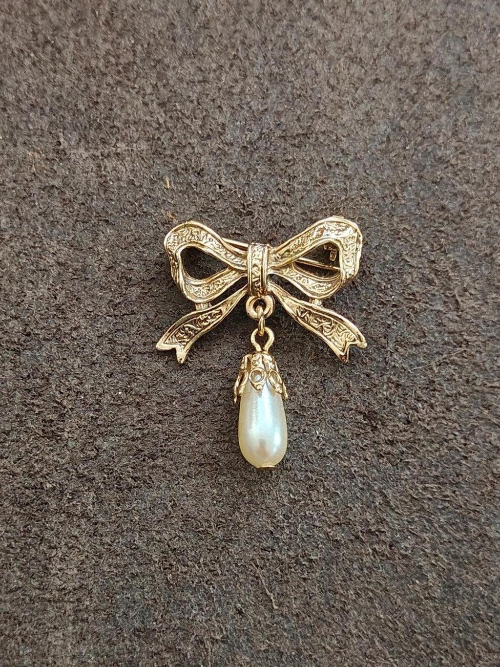 Gold Victorian-style bow brooch with embossed details and hanging faux teardrop pearl