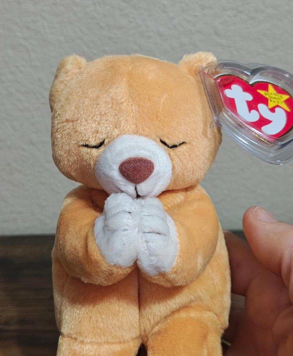 Brown plush bear with closed eyes and white praying hands, clear Ty heart tag