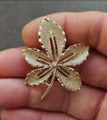 Gold-tone leaf brooch with five-point flower design and raised detail, vintage style