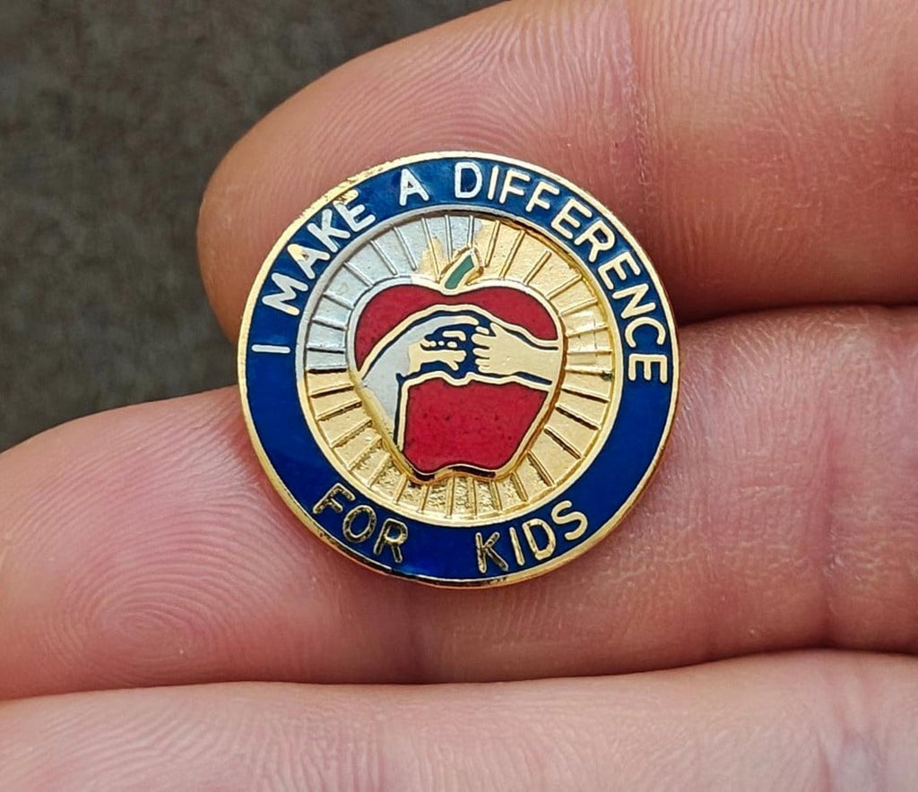 Gold-tone enamel teacher pin with blue border, “Make a Difference for Kids” text, apple icon.