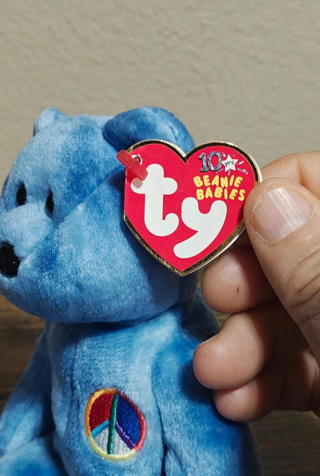 Blue bear plush with peace symbol patch and Ty heart tag held near its head