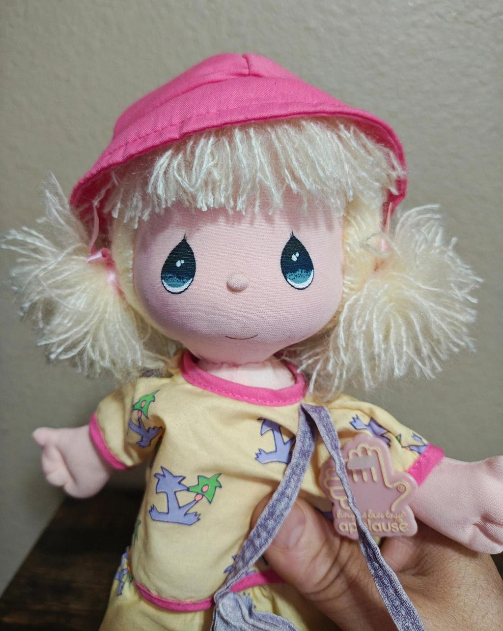 Pink plush doll face close-up with blue eyes, blonde hair, pink bucket hat and overalls