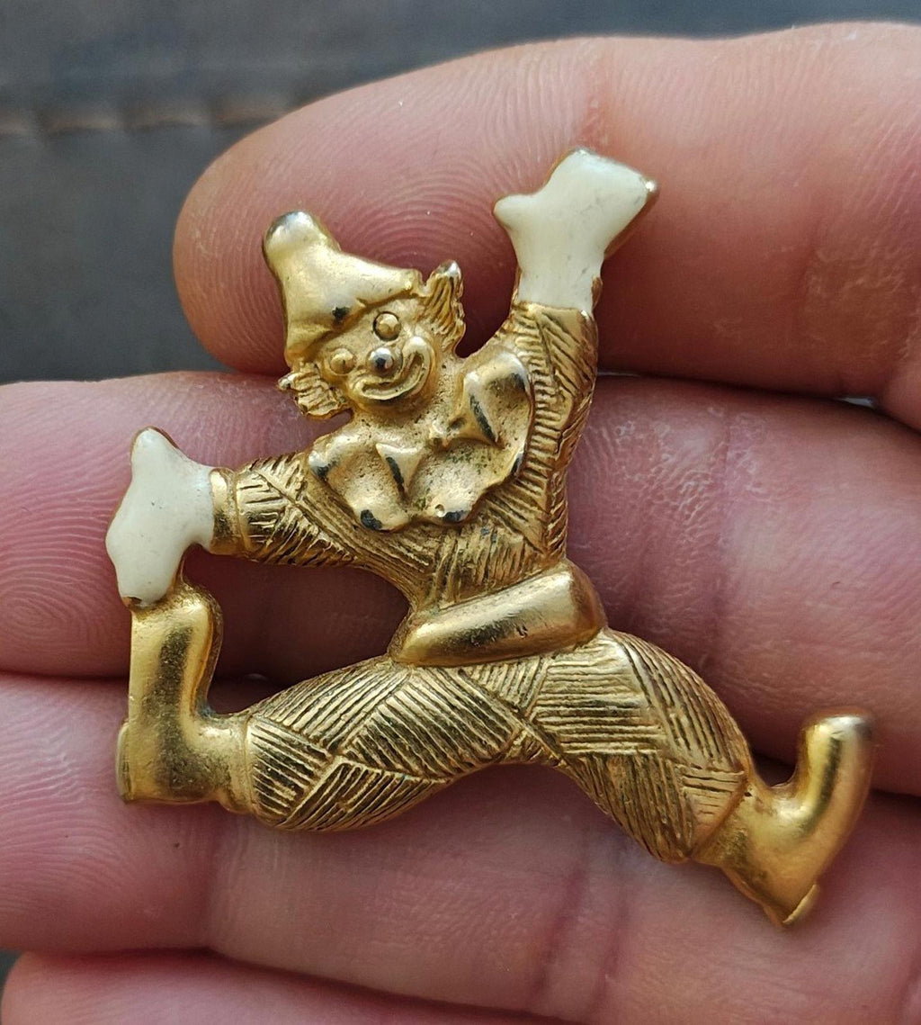 Gold tone clowning around pendant with white enamel hands and shoes, held in fingertips close-up