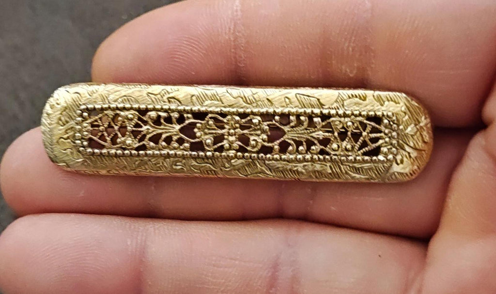 Gold tone filigree Victorian-style bar brooch held in hand, showing central decorative crest.