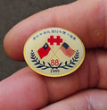 Round gold enamel national day pin with flags, 88 and 1999, laurel wreath