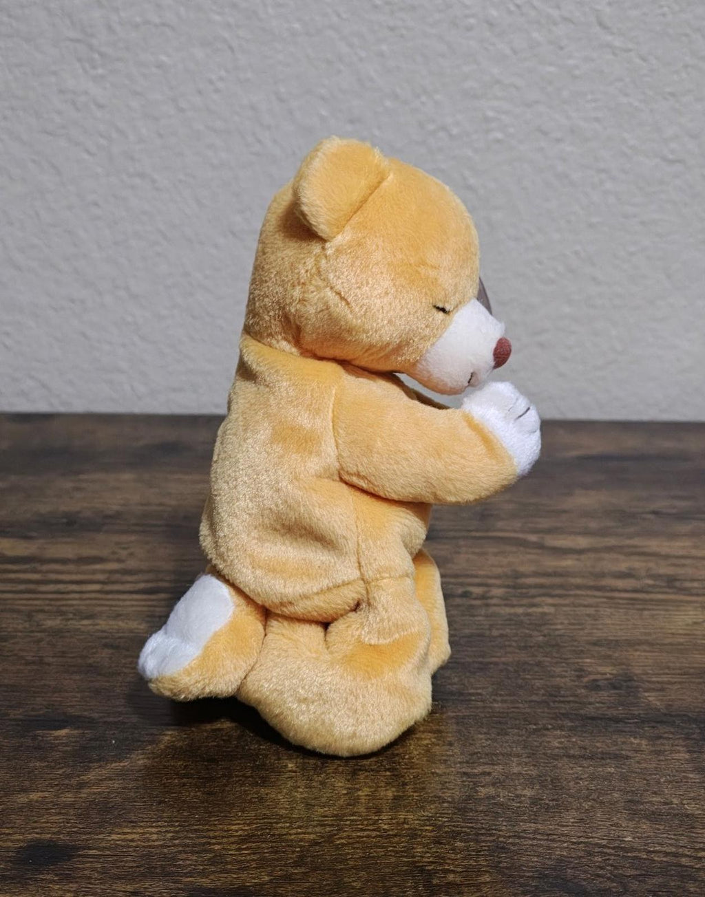 Brown plush bear kneeling in praying pose with white hands, side view