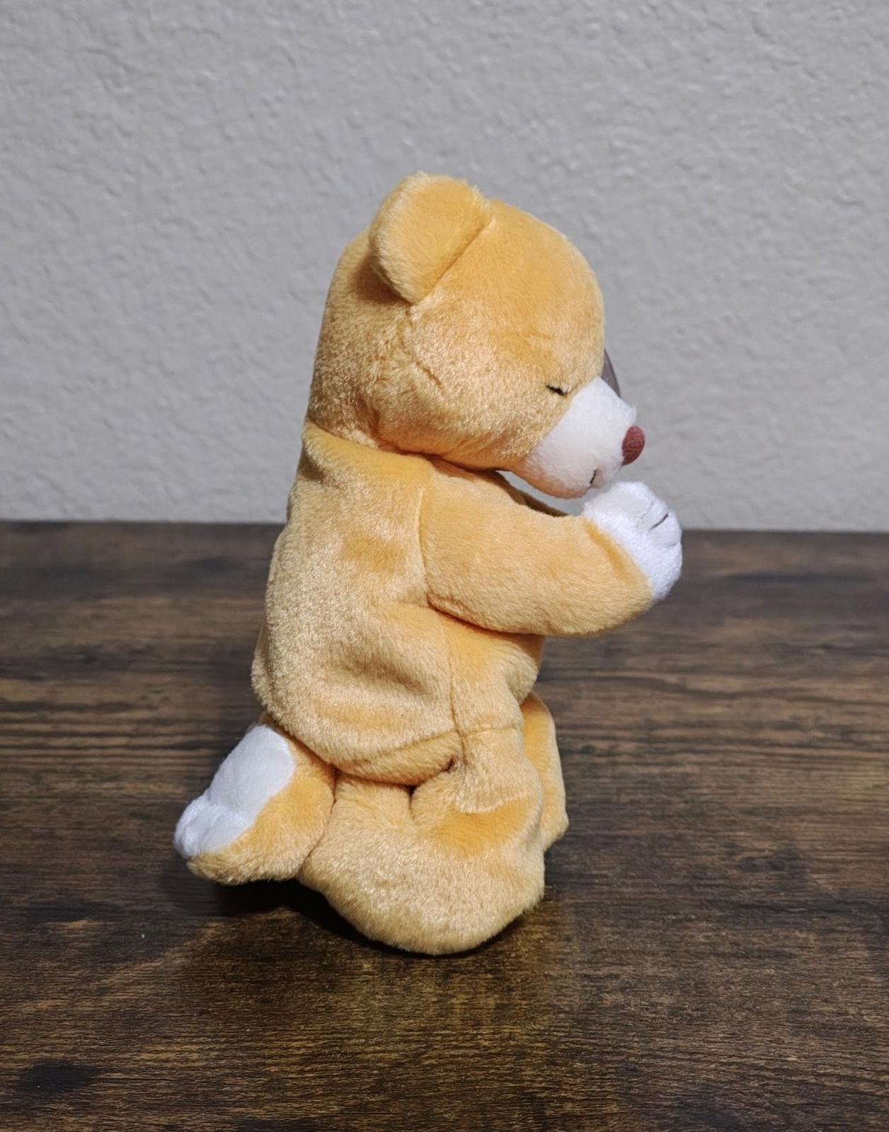 Brown plush bear kneeling in praying pose with white hands, side view