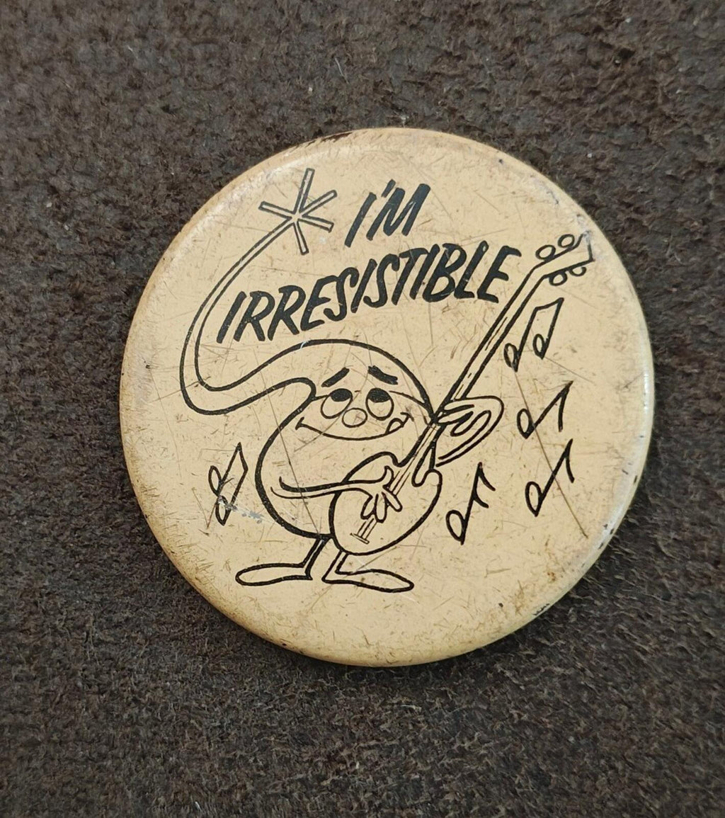 Round beige button pin with "I'm Irresistible" cartoon character holding a guitar