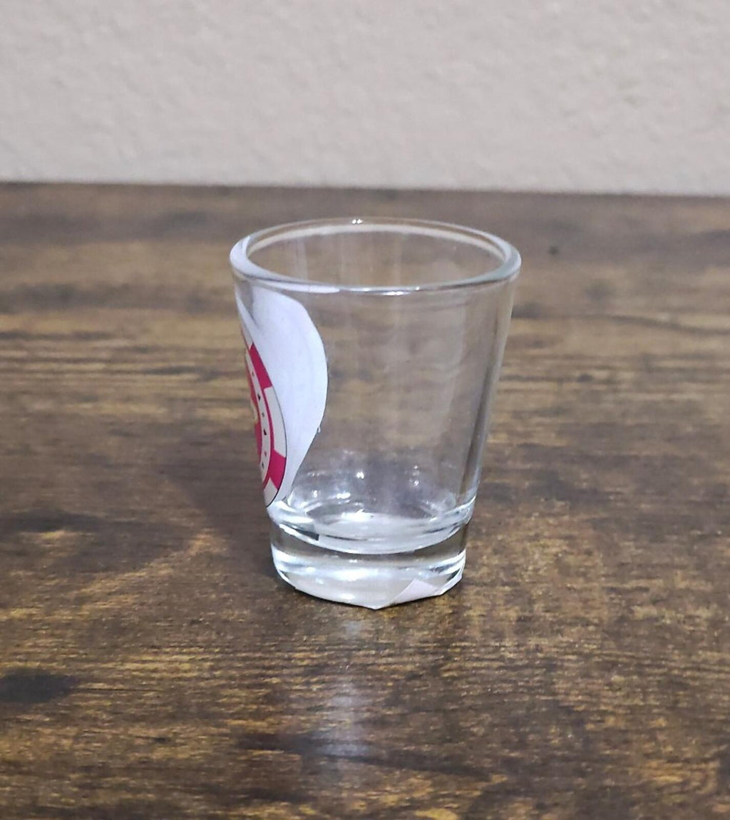 Clear shot glass on tabletop with partial pink casino chip label at the left