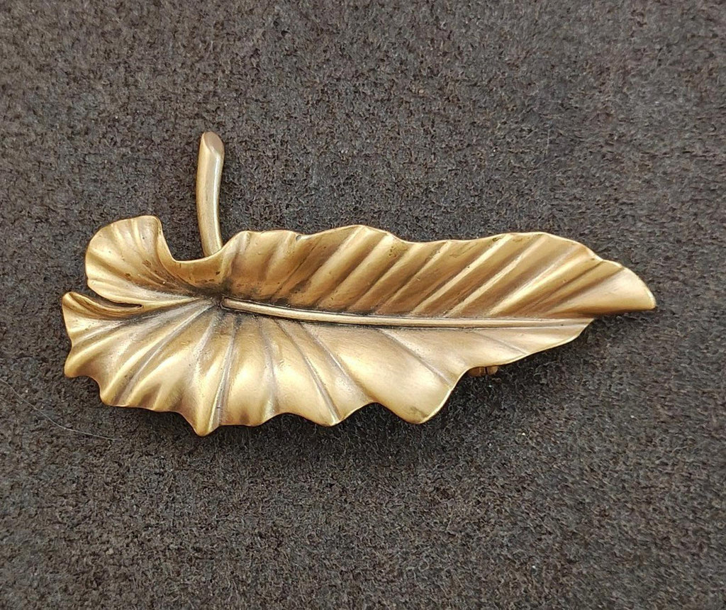 Gold-tone leaf brooch pin with textured vein lines and tall pin stem.