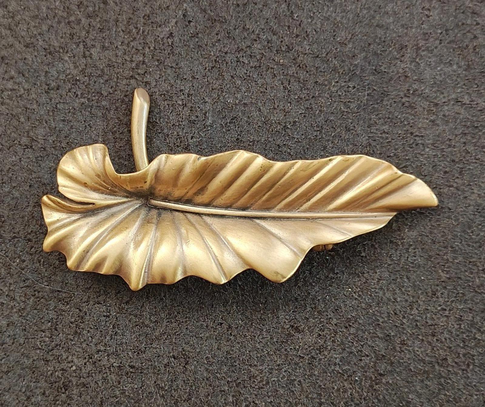 Gold-tone leaf brooch pin with textured vein lines and tall pin stem.