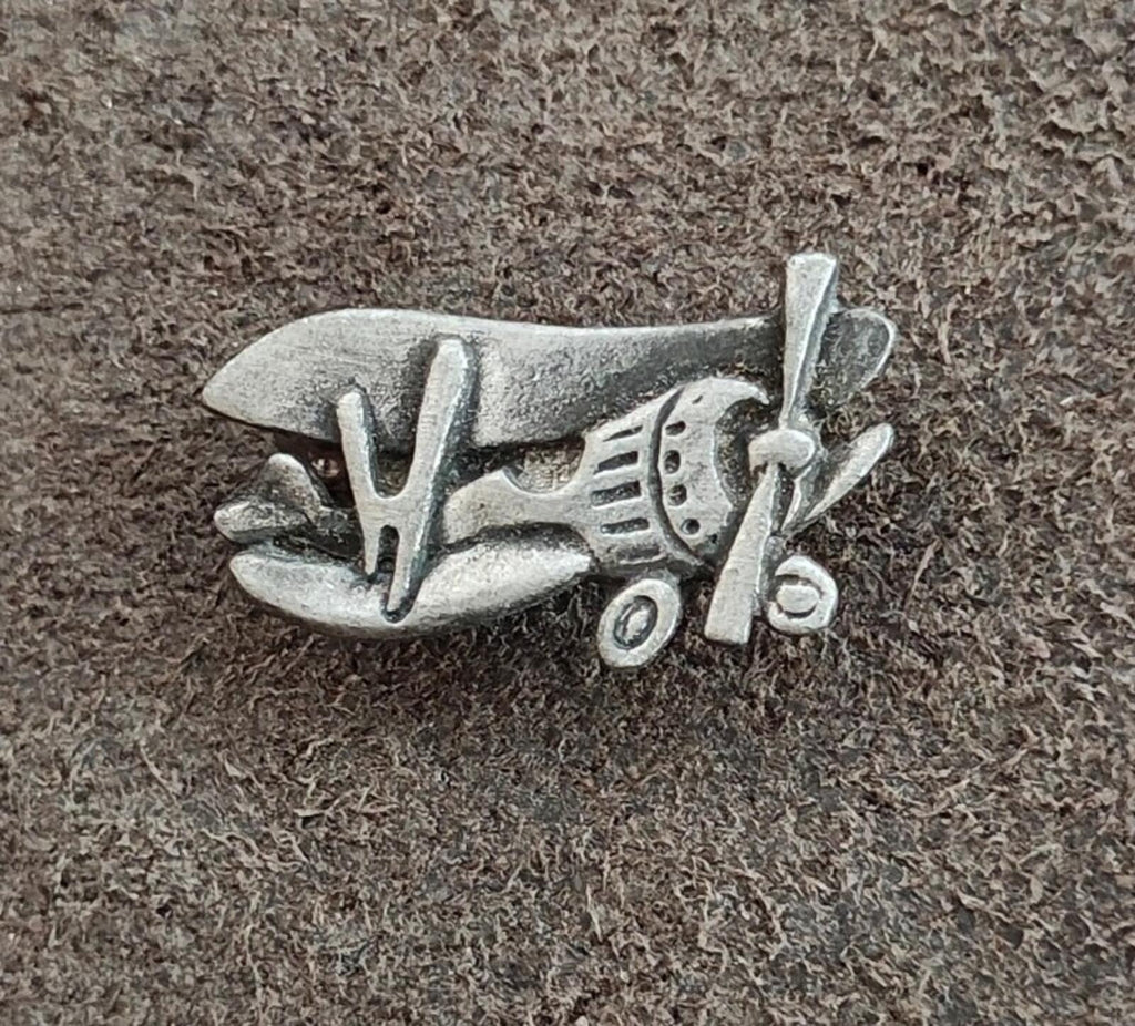 Pewter airplane brooch pin on textured background, front view with propeller and wings.