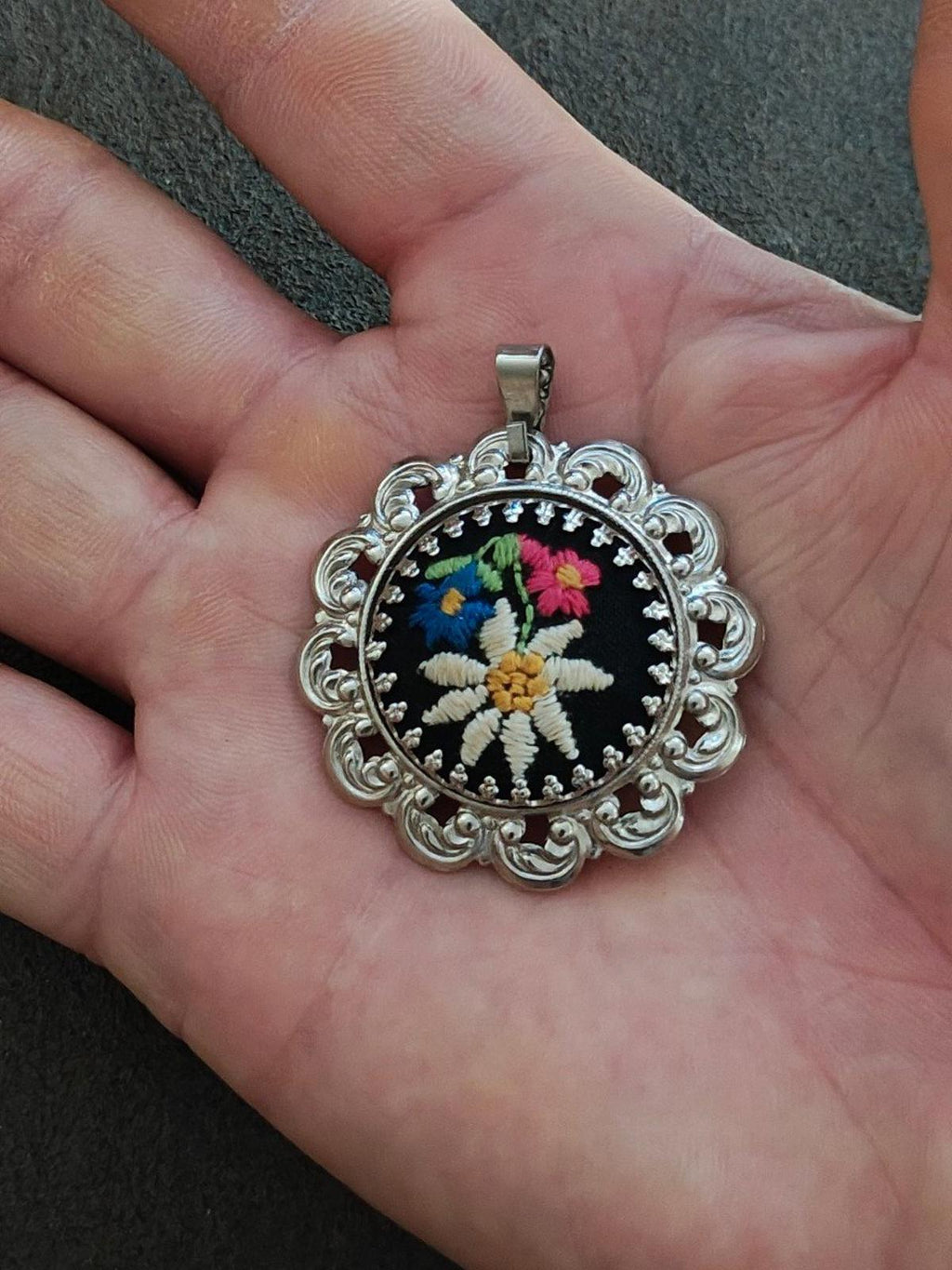 Silver filigree floral pendant featuring a round black embroidered flower on a bail.