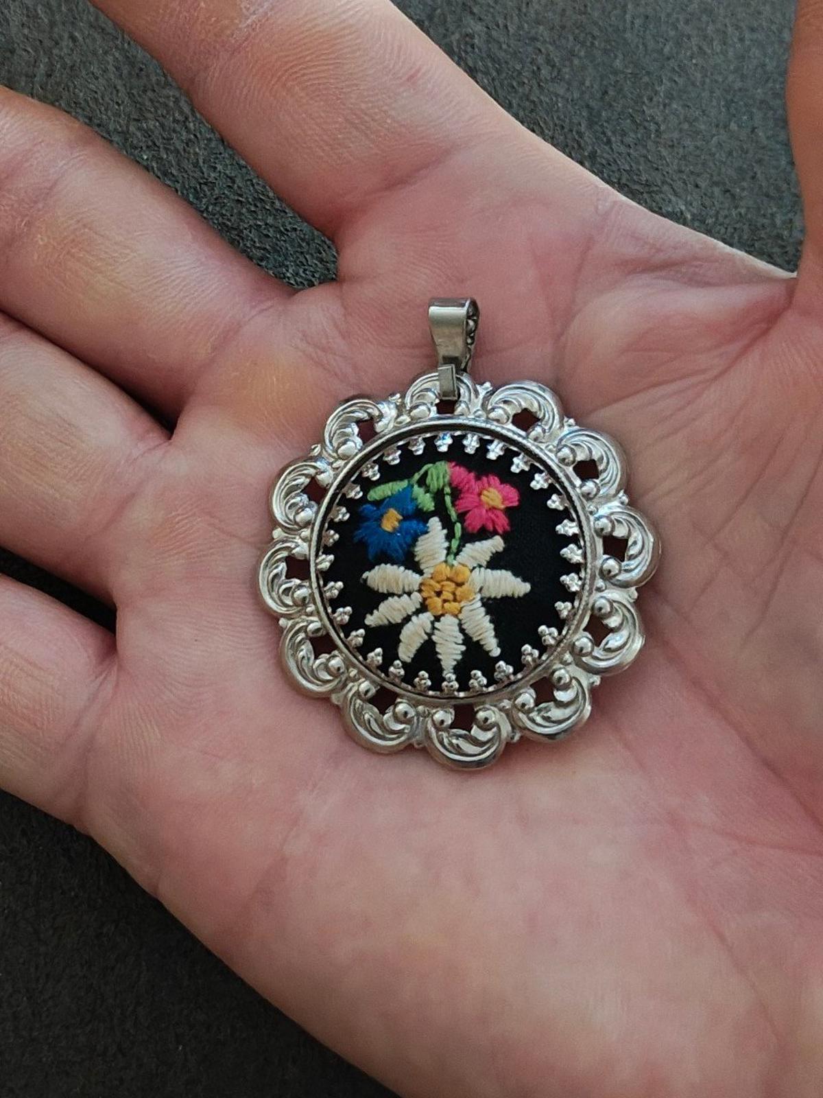 Silver filigree floral pendant featuring a round black embroidered flower on a bail.