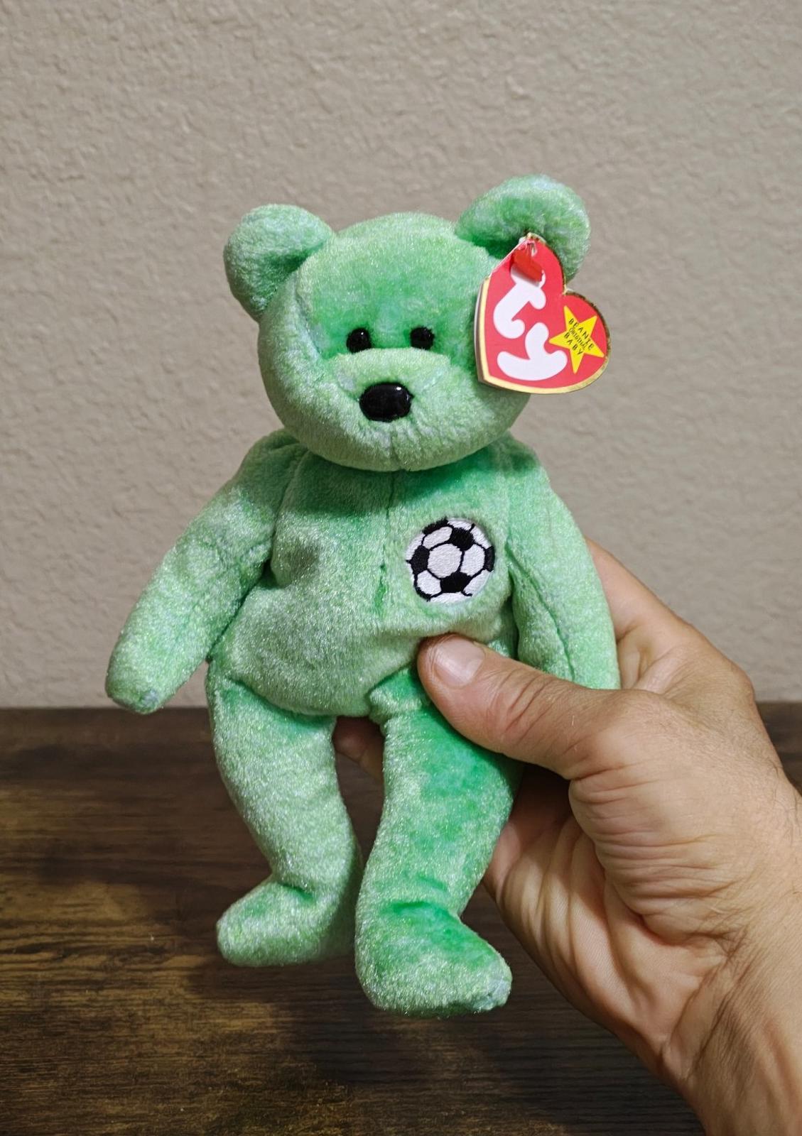 Green teddy bear plush with black nose, soccer ball patch and red TY heart tag.