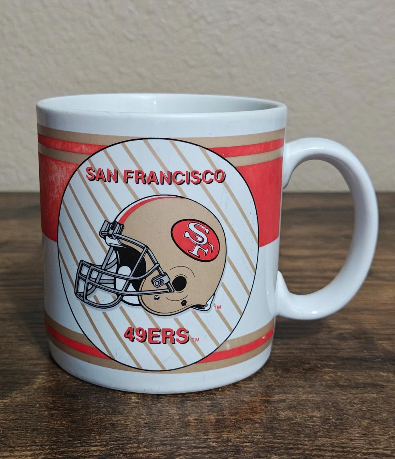 San Francisco 49ers helmet emblem mug with red horizontal stripes and striped background.