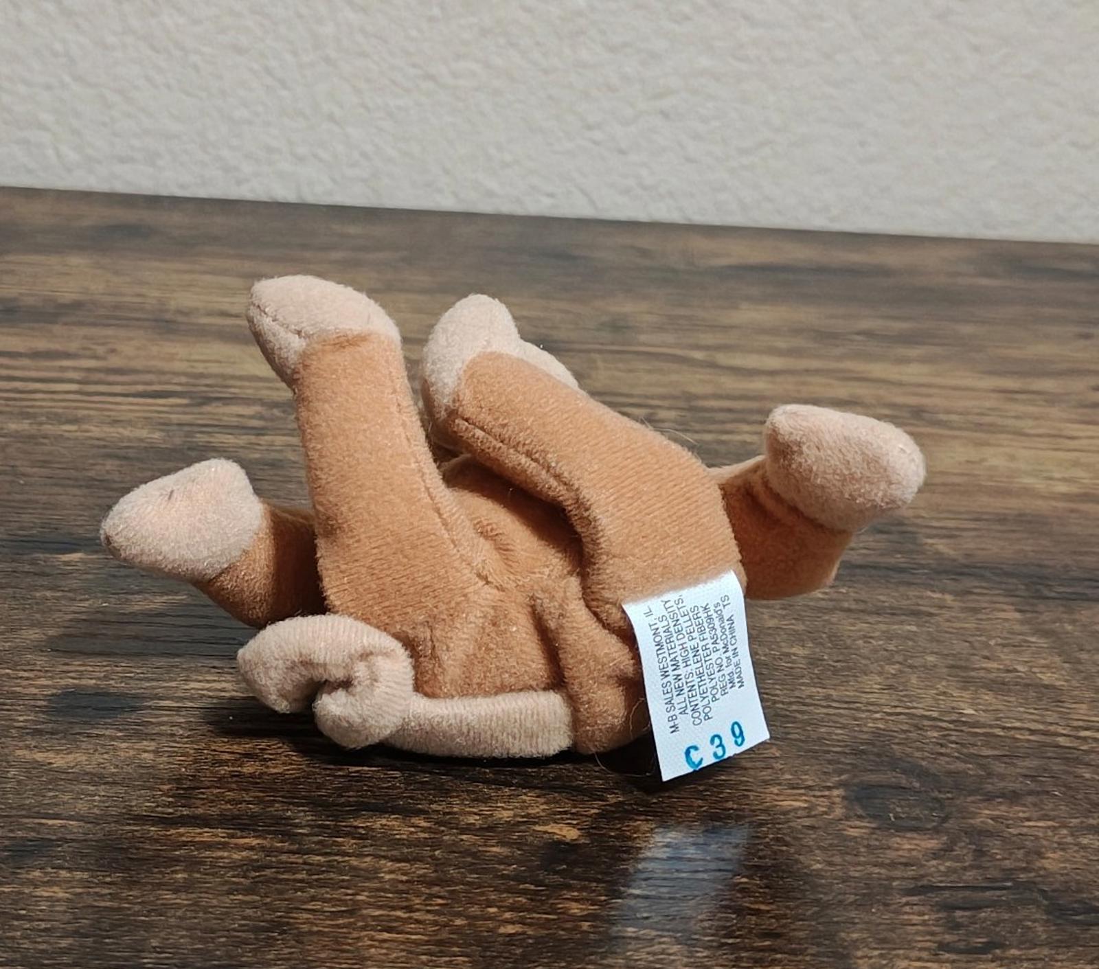 Brown plush monkey lying down with white swing tag, viewed from the side