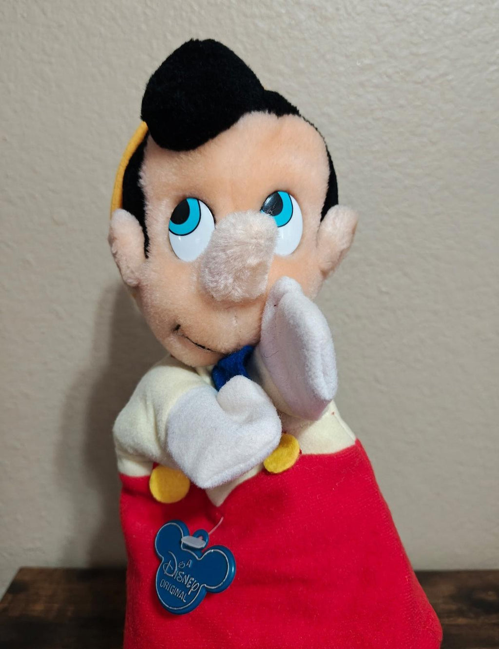 Pinocchio hand puppet with hands clasped near face, red overalls and blue bow