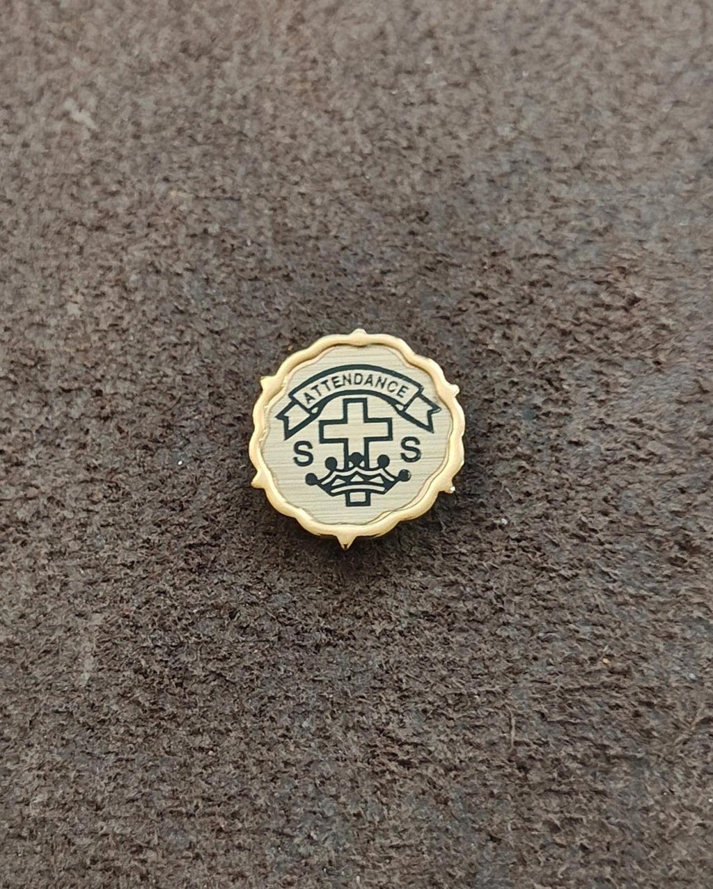 Gold-tone attendance pin featuring a cross, S marks, and a crown-like emblem.