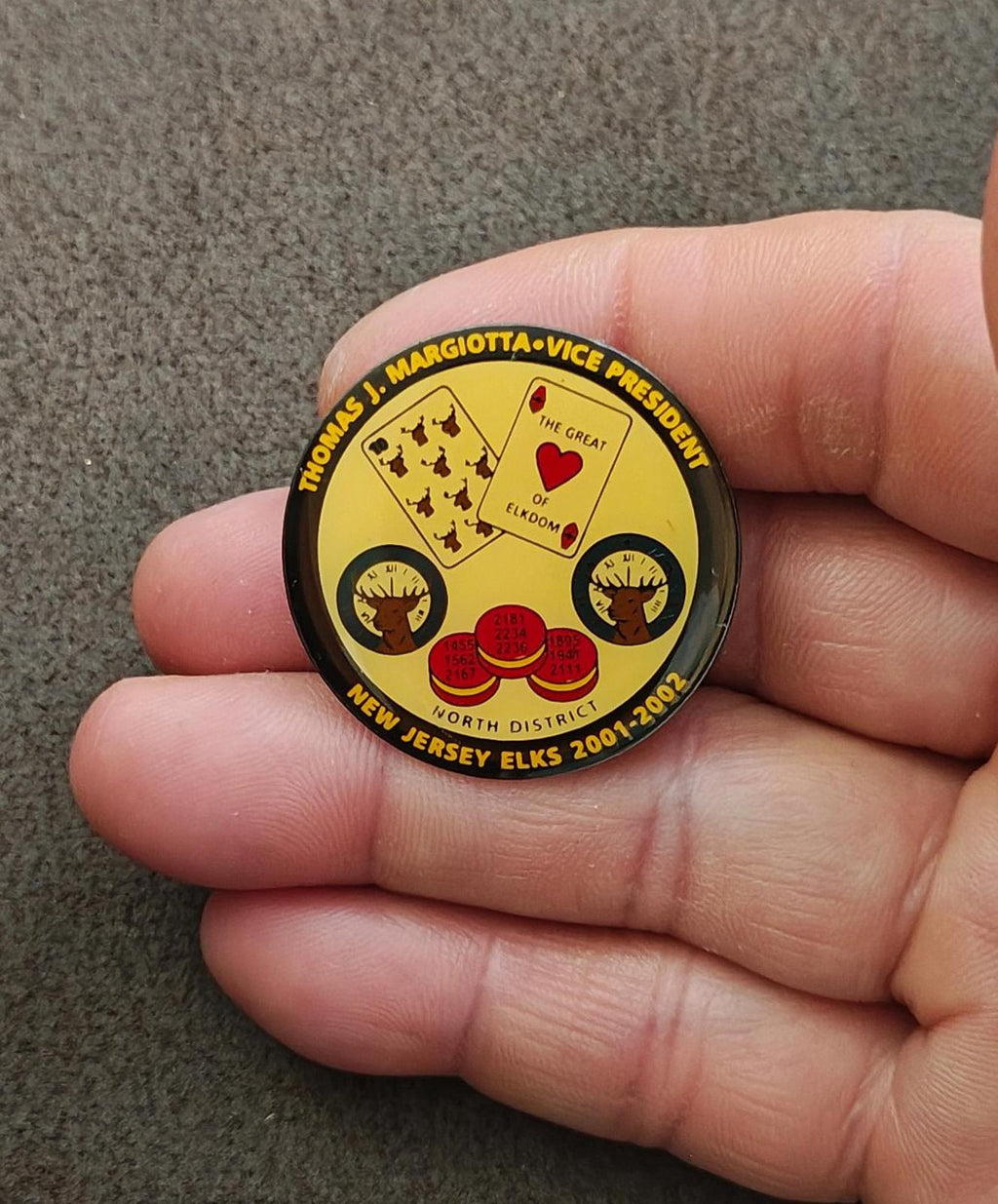 Gold tone lapel pin with yellow emblem and black edge, held in a hand.