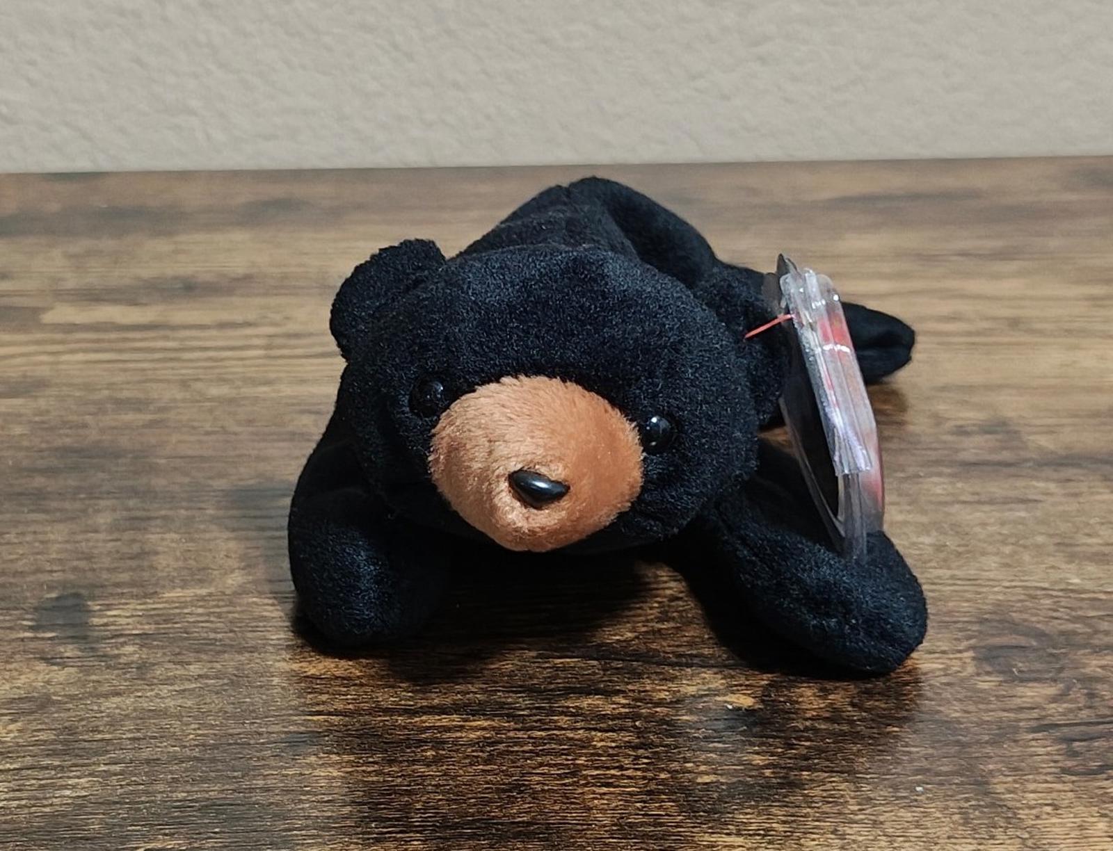 Black plush bear beanbag lying on its belly, tan snout and clear tag attached