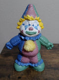 Hand-painted porcelain clown figurine with blue, green, and pink suit, seated pose.