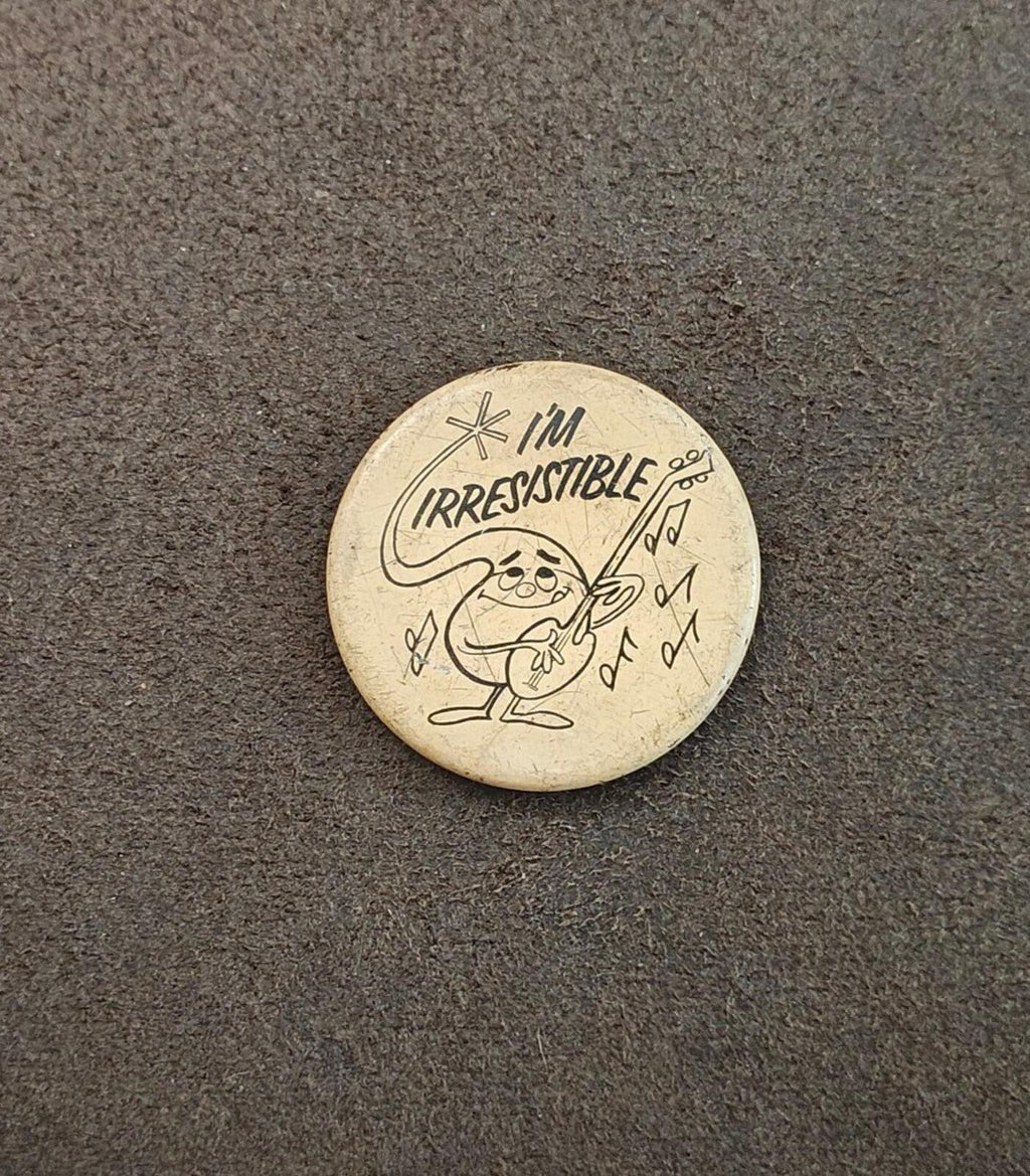 Small round beige button pin with "I'm Irresistible" cartoon design