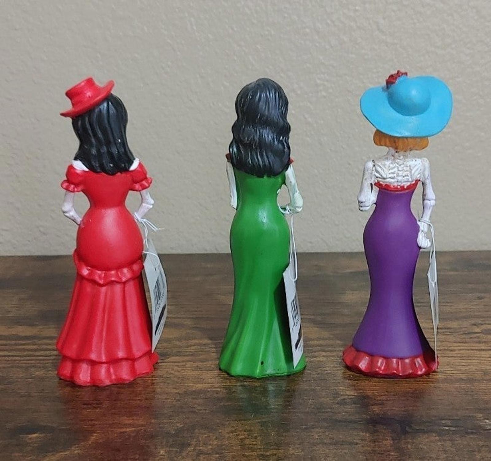 Three Catrina figurines back view, red, green, and purple dresses