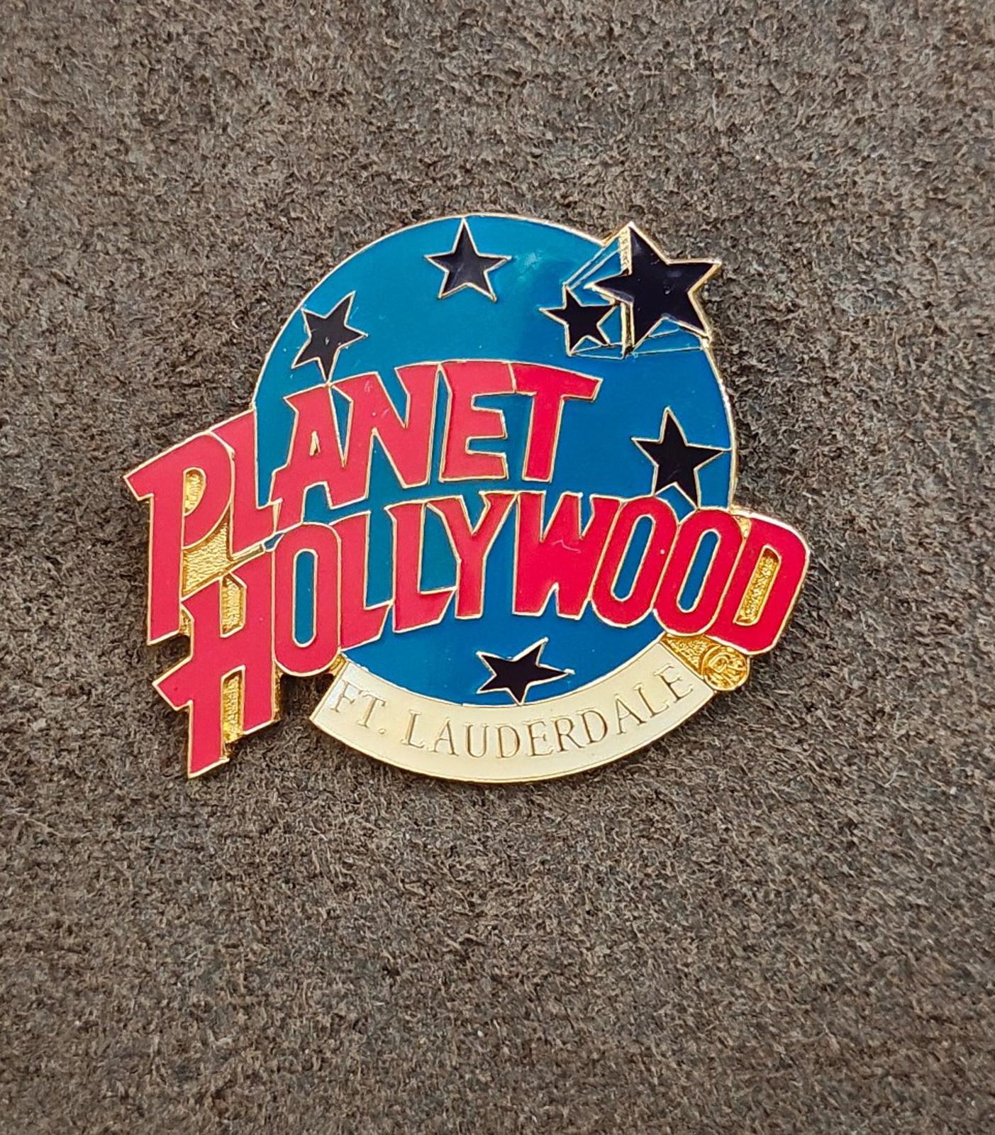 Blue enamel lapel pin with red Planet Hollywood lettering, star icons, gold rim.
