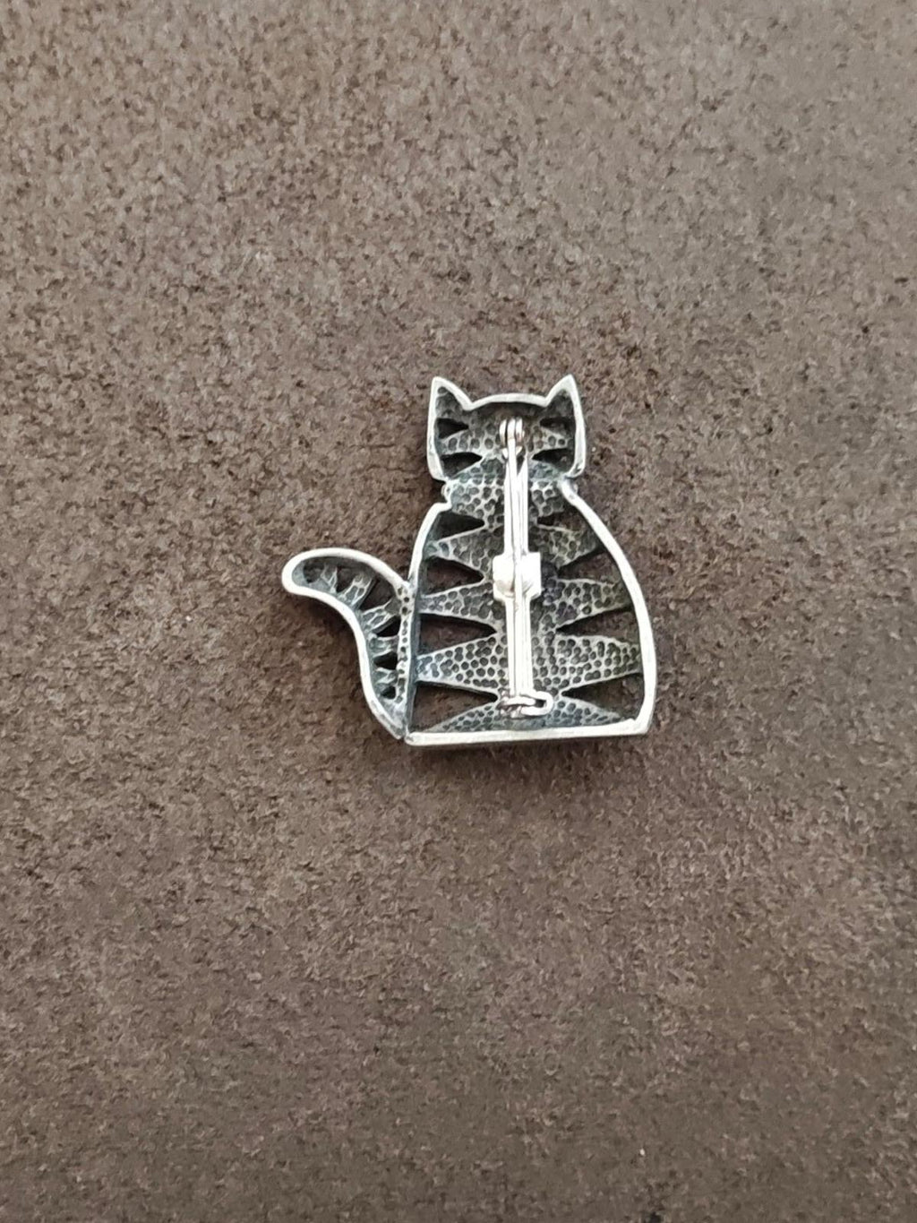 Silver cat brooch back view with safety clasp and textured finish, on gray surface