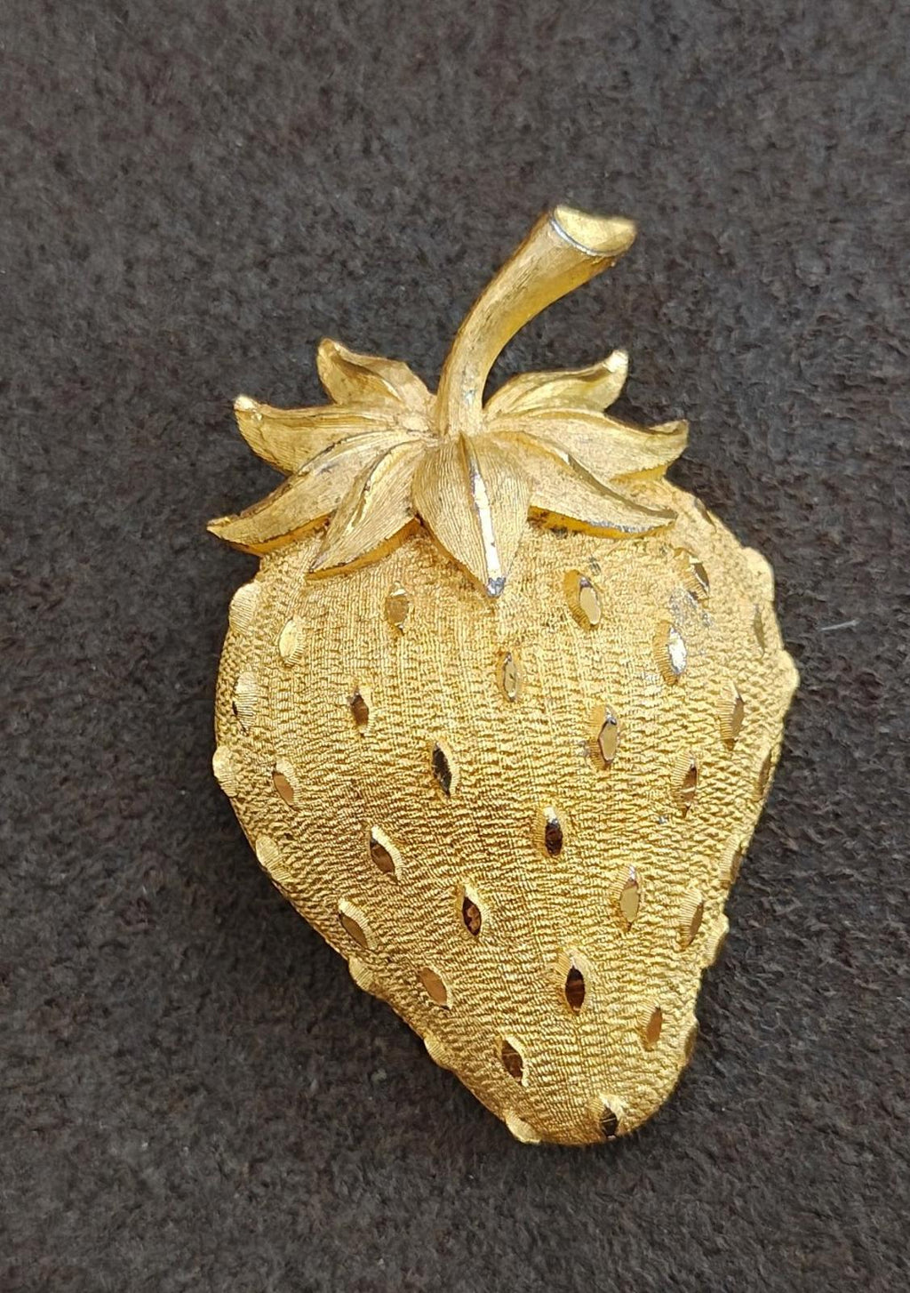 Gold tone strawberry brooch pin, front view with stem and leaf cluster, dotted texture.