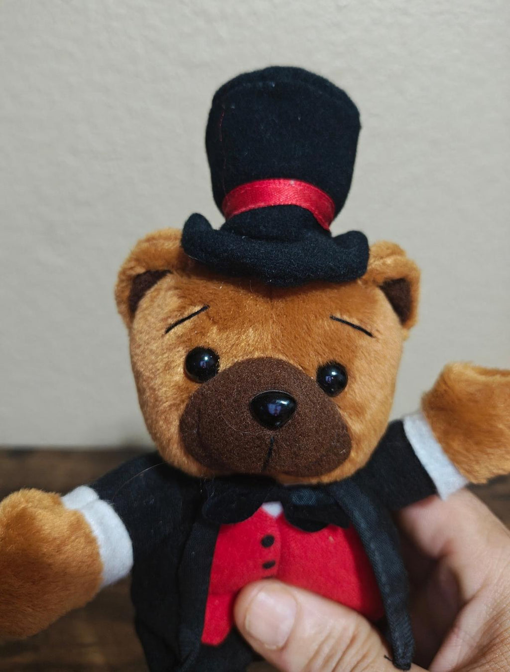 Plush bear face wearing a black top hat with red band, black bow tie, red vest.