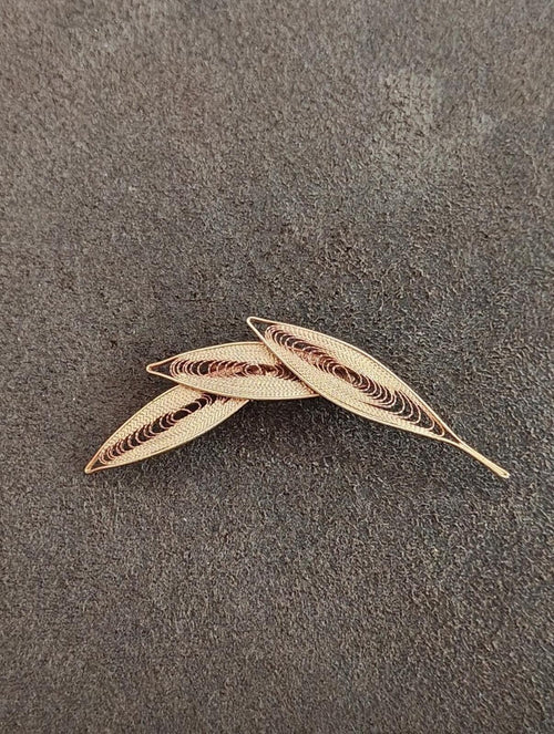 Gold filigree leaf brooch with openwork oval detailing, laid on dark surface