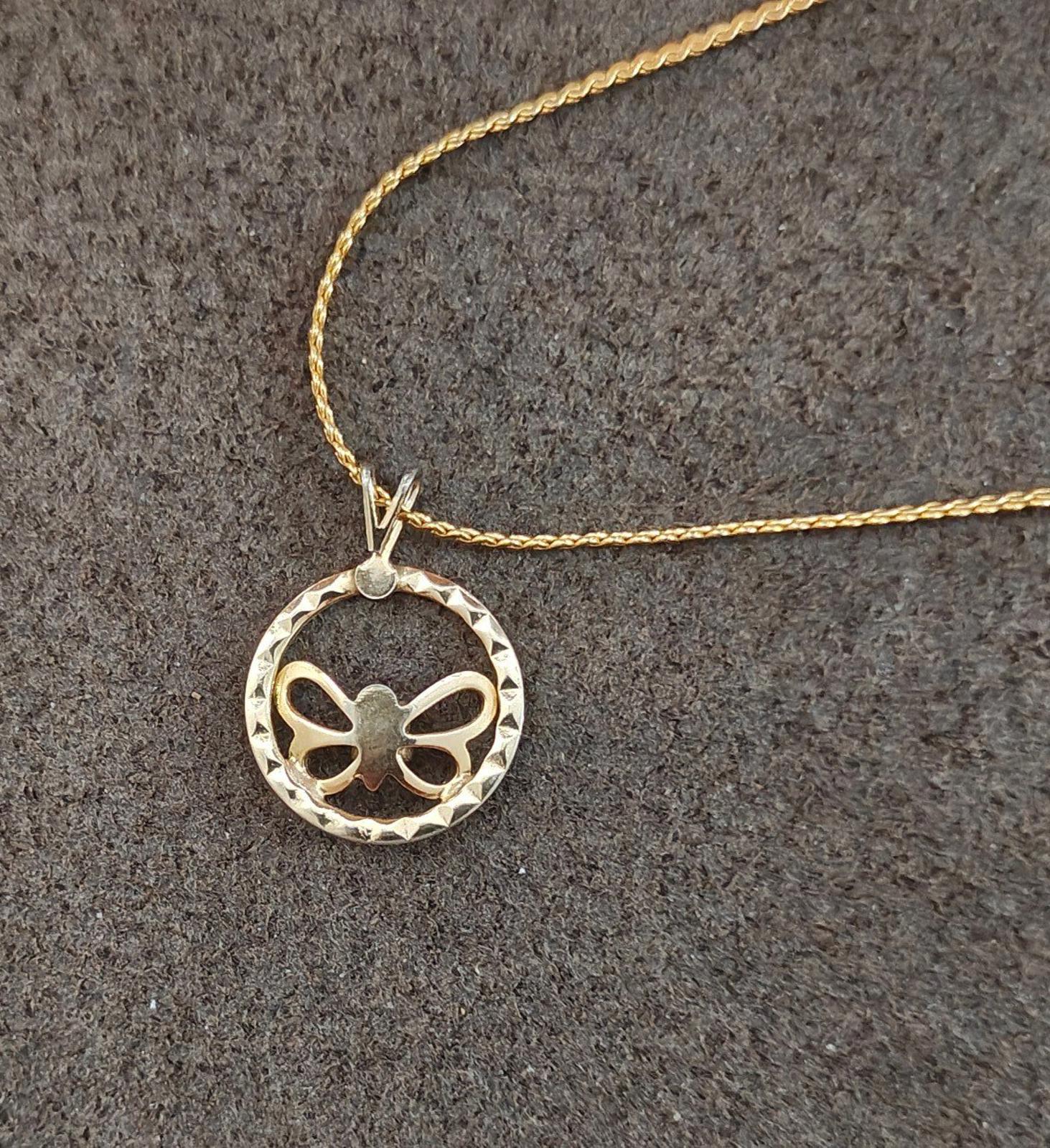 Gold-tone pendant necklace close-up: round open circle with butterfly bow and clear rhinestone