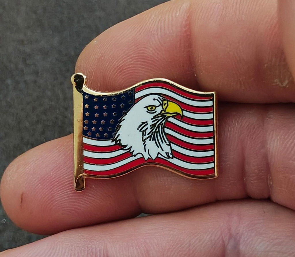 Gold-tone enamel wavy American flag lapel pin with bald eagle, held between fingers