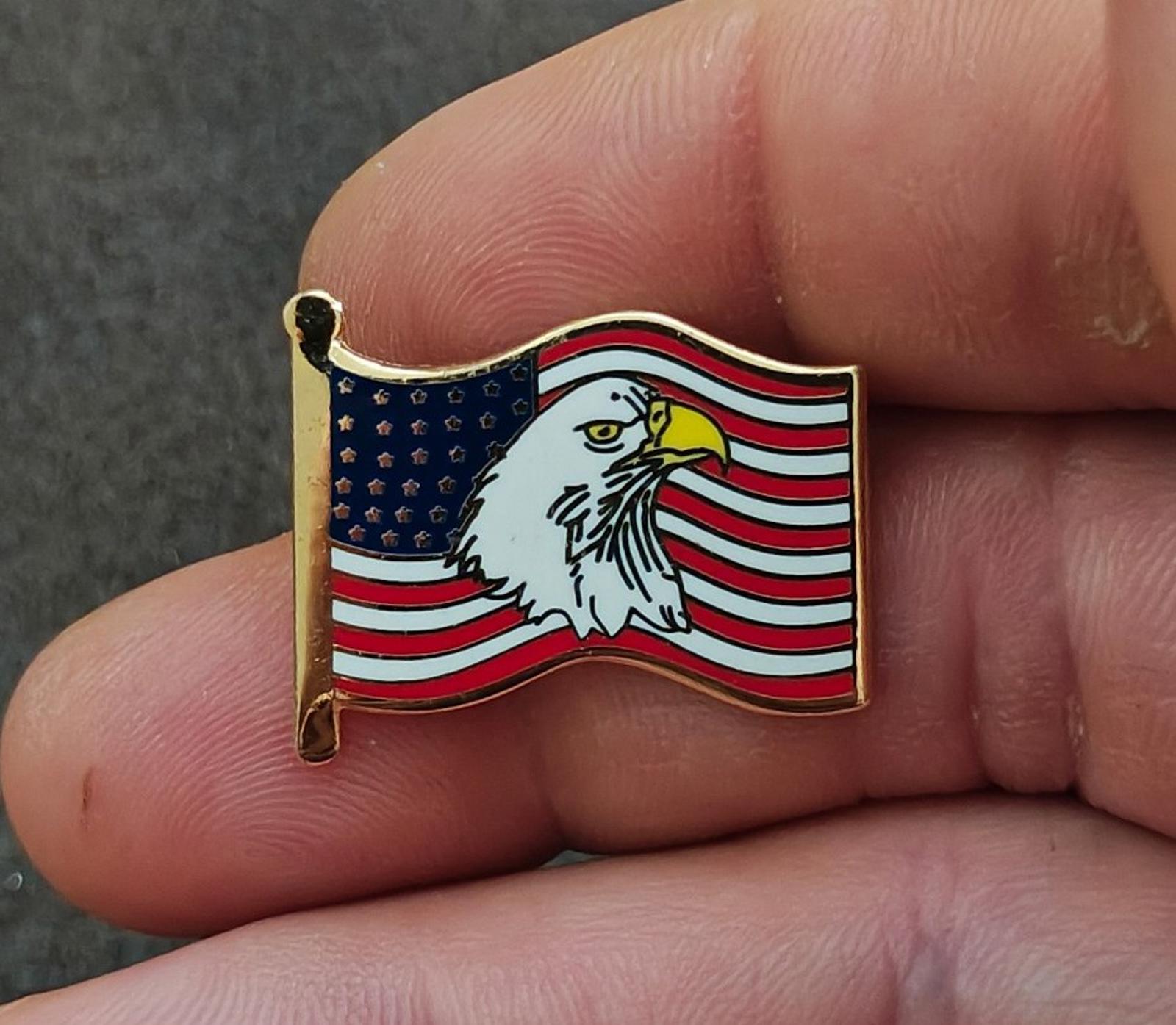 Gold-tone enamel wavy American flag lapel pin with bald eagle, held between fingers