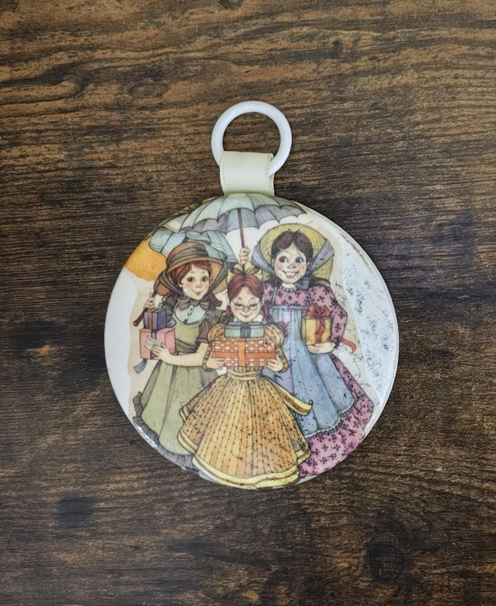 Round ornament with illustrated three girls in prairie dresses, centered hanging loop