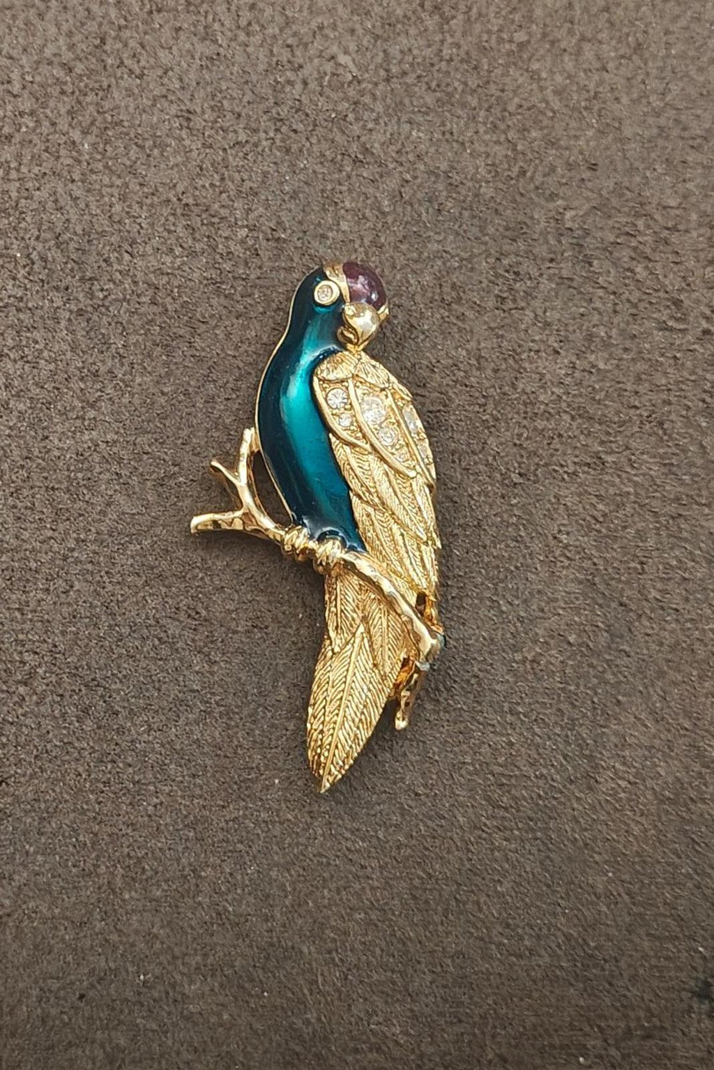 Gold tone enamel bird brooch on a surface, teal body with rhinestones and purple head gem