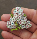 Gold-tone floral rhinestone brooch with white petals, pink and blue accents, and green leaves